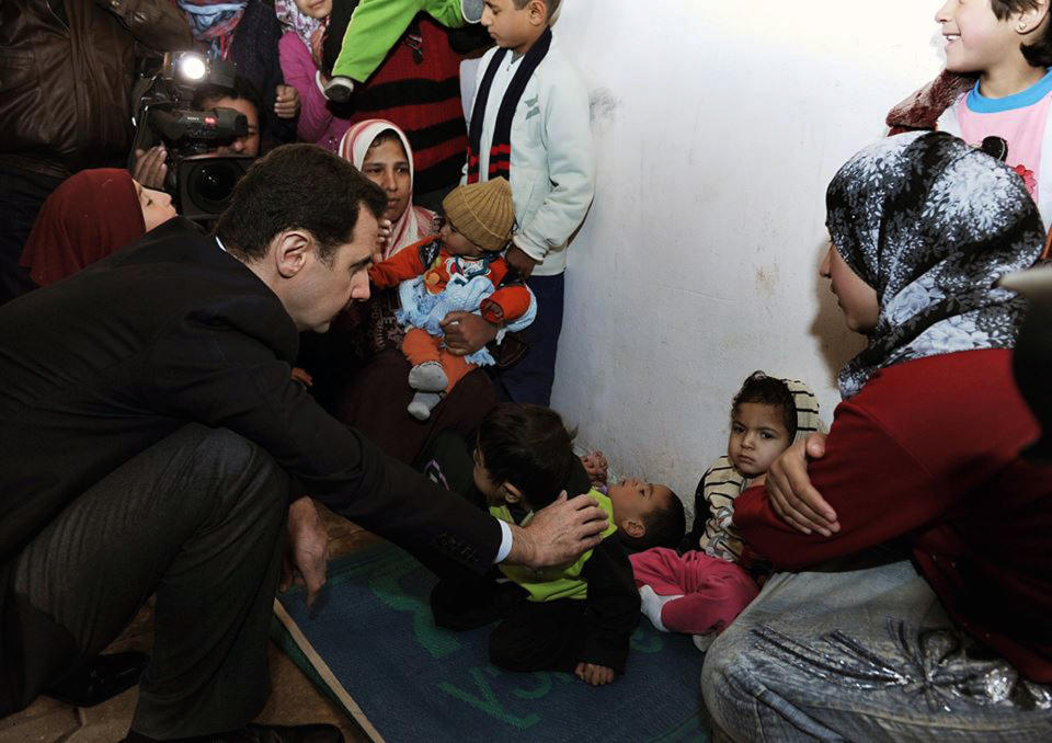 In this photo released on the official Facebook page of Syrian Presidency, Syrian president Bashar Assad, center left, visits a shelter of internally displaced people in the Damascus suburb of Adra, Syria, Wednesday, March 12, 2014. Syria's state TV reported that President Bashar Assad made a rare public appearance, visiting people displaced by the war in the suburb. Syrian troops have been on the offensive in Adra, just northeast of Damascus, after rebels captured parts of it in December, which displaced thousands from the area. A July U.N. estimate said 6.5 million have been uprooted from their homes and displaced within Syria. (AP Photo)