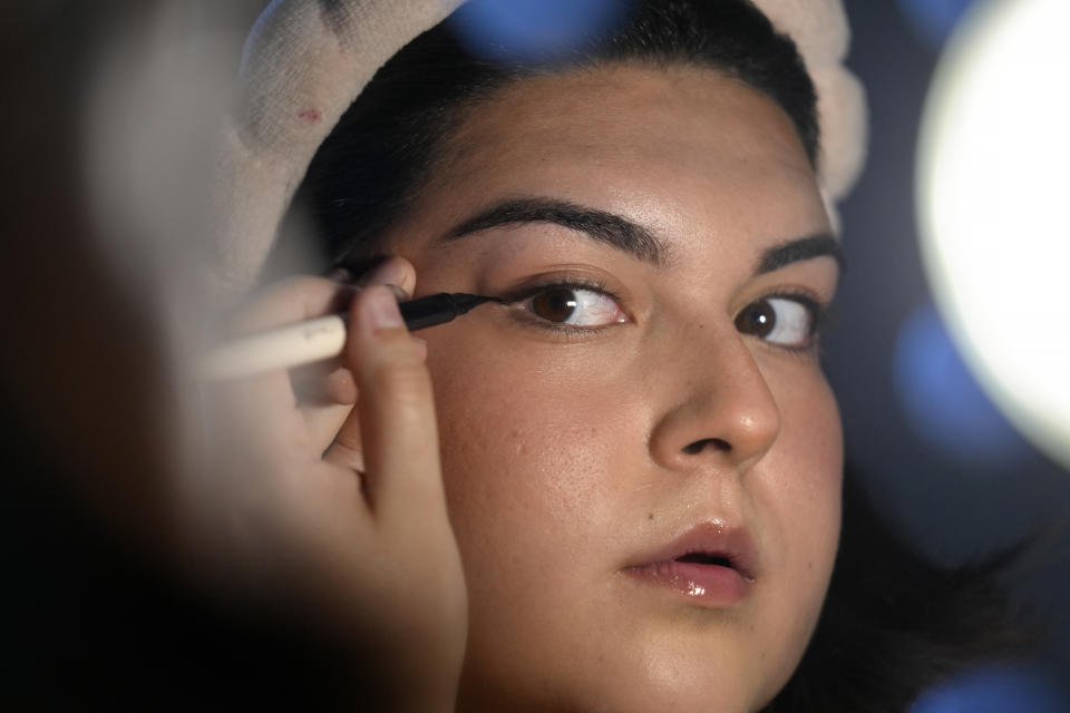 Daniella López White, of Hawaii, uses a mirror while applying makeup, Tuesday, May 14, 2024, at her apartment in Boston. López White, who graduated from Emerson College in Boston this month and is on a tight budget, said TikTok influencers have helped her with tips on how to find affordable clothes at places like H&M and thrift shops. She buys makeup brands at CVS based on influencer advice. (AP Photo/Steven Senne)