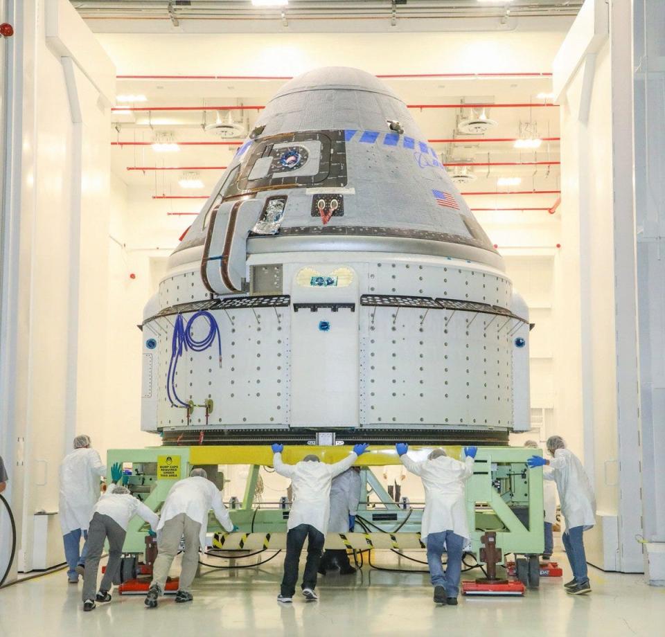 technicians roll boeing starliner spaceship down hallway