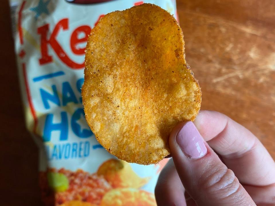 hand holding chip in front of bag of aldi nashville hot chicken chips