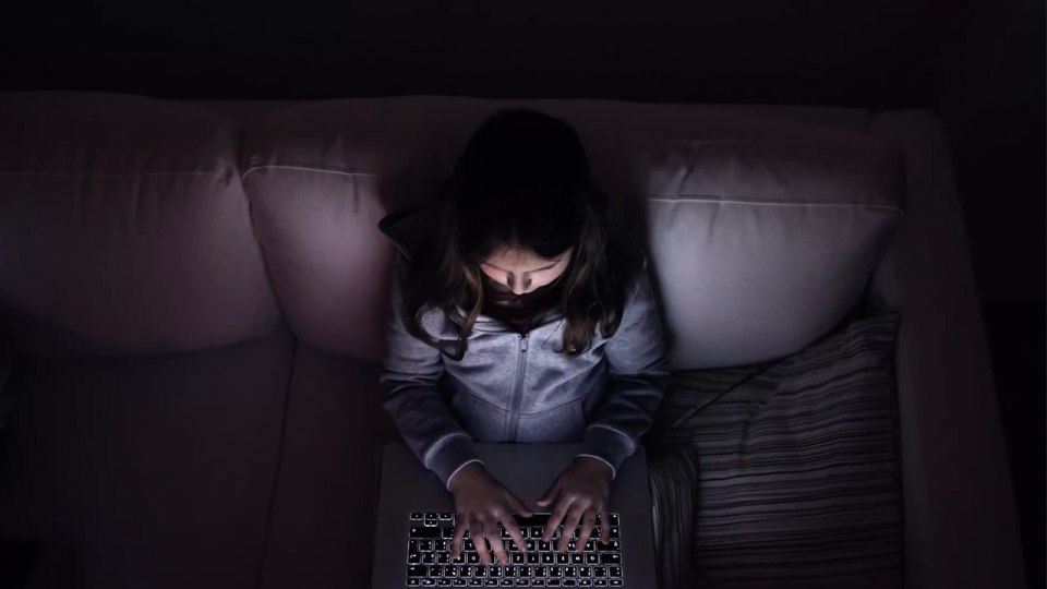 Little girl, sitting in a dark, playing with laptop .