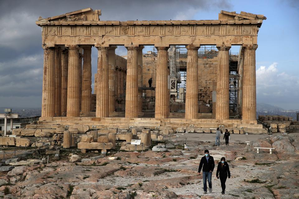 The first visitors wearing face masks to protect against the spread of coronavirus, walk atop of Acropolis hill, as the Parthenon temple is seen in the background in Athens, Monday, March 22, 2021. Greece's government reopened the Acropolis and other ancient sites nationwide after four months as it prepares to restart the tourism season in mid-May. (AP Photo/Thanassis Stavrakis)