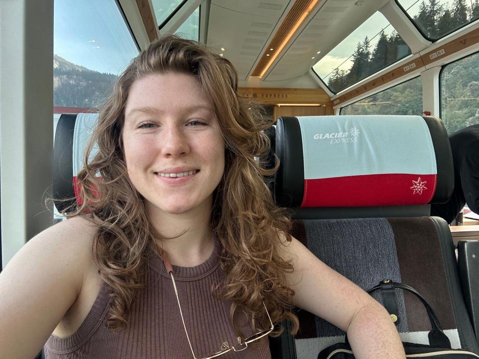 selfie smiling woman sitting on a train with panoramic windows and pine trees outside