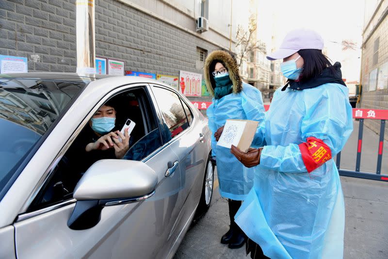 Resident scans a QR code held by a volunteer at the gate of a residential compound in Xinle, Shijiazhuang