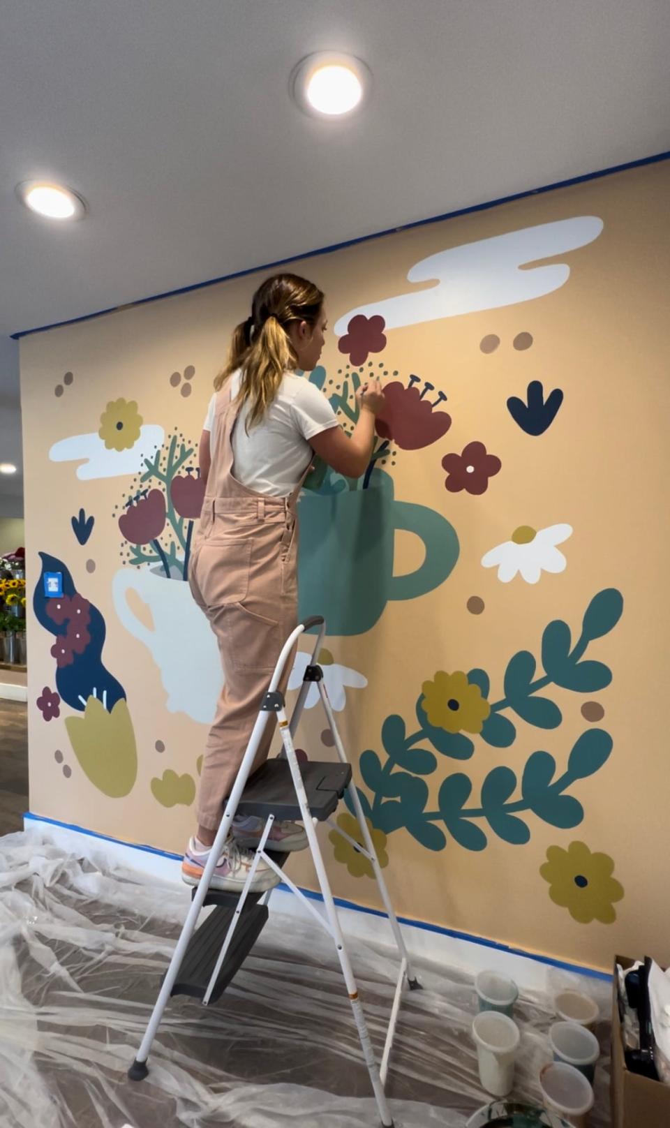 Illustrator Paris Woodhull installs a mural at Cultivate in Fountain City. “I feel like so many people say they are not an artist, but it is about your interest level,” she said. “You can have natural talent, but most of it comes from really focusing on what you do like to do.”