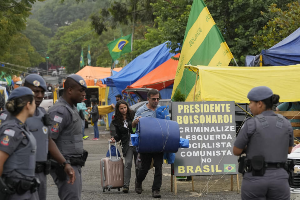 Supporters of former Brazilian President Jair Bolsonaro leave their encampment outside army headquarters as military police stand watch in Sao Paulo, Brazil, Monday, Jan. 9, 2023, the day after Bolsonaro supporters stormed government buildings in the capital. (AP Photo/Andre Penner)