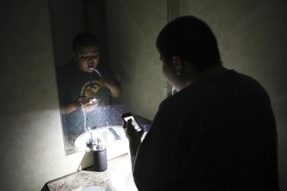 In this Wednesday, May 8, 2019 photo, Jayden Long, 13, brushes his teeth by cell phone light in the bathroom of his home on the Navajo Reservation. Long has spent more than a decade living with his family in a home with no electricity relying on a generator for power. An ambitious project to connect homes to the electric grid on the country's largest American Indian reservation is wrapping up Utility crews from across the U.S. have volunteered their time over the past few weeks to hook up about 300 homes on the Navajo Nation. (AP Photo/Jake Bacon)