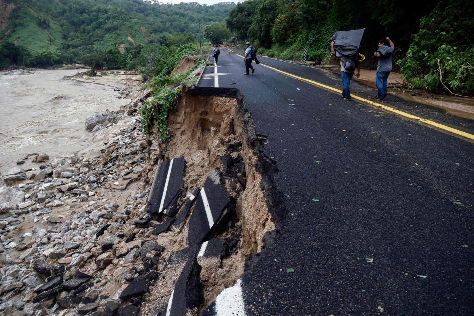 People pass by part of a road which was washed away at the Kilometro 42 community, near Acapulco (AFP via Getty Images)