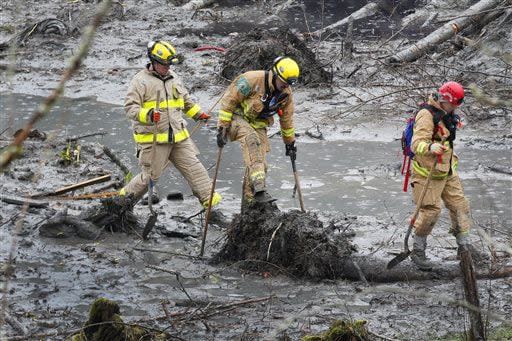 Firefighters carefully cross a pool of water, using a fallen tree as a path, at the west side of the mudslide on Highway 530 near mile marker 37 on Sunday, March 30, 2014, in Arlington, Wash. Periods of rain and wind have hampered efforts the past two days, with some rain showers continuing today. (AP Photo/Rick Wilking, Pool)