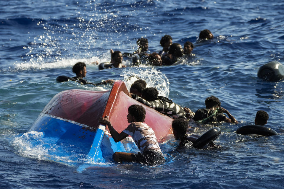 FILE - Migrants swim next to their overturned wooden boat during a rescue operation by Spanish NGO Open Arms at south of the Italian Lampedusa island at the Mediterranean sea, Aug. 11, 2022. Italy's new government has blocked humanitarian rescue ships from accessing its ports, resulting in a stand-off with charities that patrol the deadly central Mediterranean Sea smuggling routes, used by people desperate to reach Europe for a new life. (AP Photo/Francisco Seco, file)