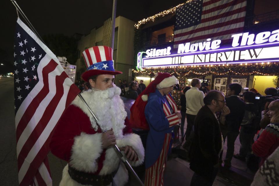 Matt Ornstein, dressed in a Santa Claus costume, holds an American flag as fans line up at the Silent Movie Theatre for a midnight screening of "The Interview" in Los Angeles, California December 24, 2014. "The Interview," the provocative comedy that triggered a devastating cyber attack on Sony Pictures, went straight to U.S. consumers on Wednesday in an unprecedented online debut on Wednesday. REUTERS/Jonathan Alcorn (UNITED STATES - Tags: POLITICS ENTERTAINMENT)