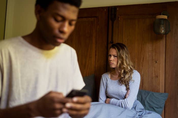 Man focused on his phone while a woman sits behind him looking upset or concerned