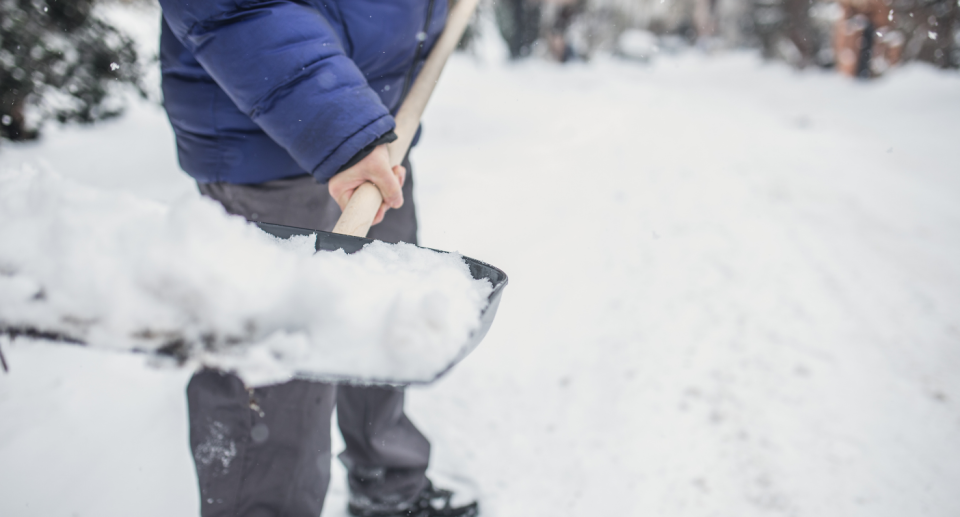 man shovelling snow in blue puffer jacket and grey pants 