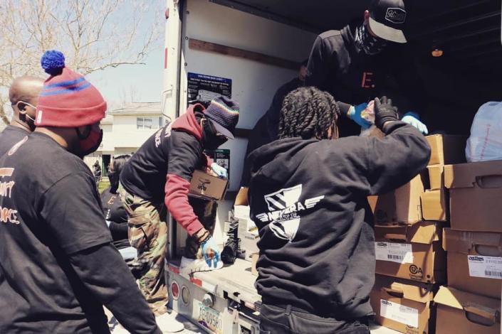 Four members of New Era Detroit gather behind a truck as another passes down boxes of food to give to seniors.