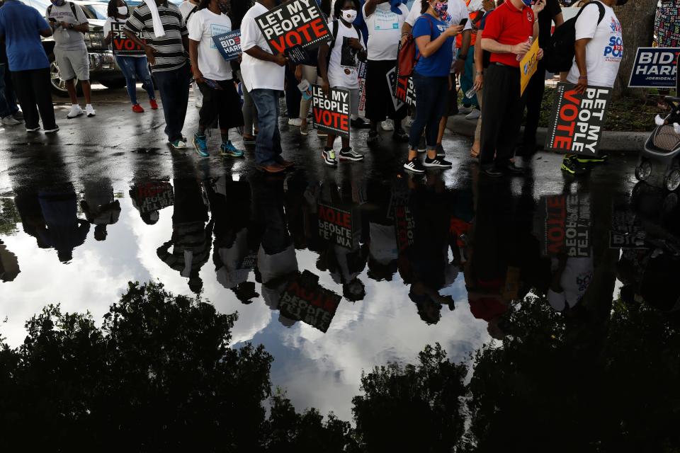 People carrying signs supporting voting rights are reflected in a puddle as they arrive at an early voting center at Model City Branch Library, as part of a "Souls to the Polls" march, in Miami, Sunday, Nov. 1, 2020. As Election Day closes in, Americans are exhausted from constant crises, on edge because of volatile political divisions and anxious about what will happen next.(AP Photo/Rebecca Blackwell)