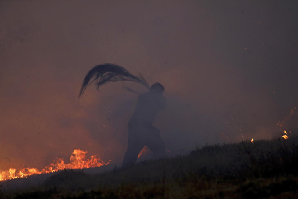 A volunteer is engulfed in smoke while using a tree branch to try to stop a wildfire in Gouveia, in the Serra da Estrela mountain range, in Portugal on Thursday, Aug. 18, 2022. Authorities in Portugal said Thursday they had brought under control a wildfire that for almost two weeks raced through pine forests in the Serra da Estrela national park, but later in the day a new fire started and threatened Gouveia. (AP Photo/Joao Henriques)