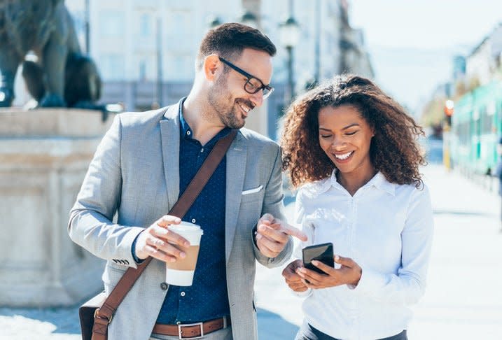 Two happy friends look at something on a phone outside in the city during the day