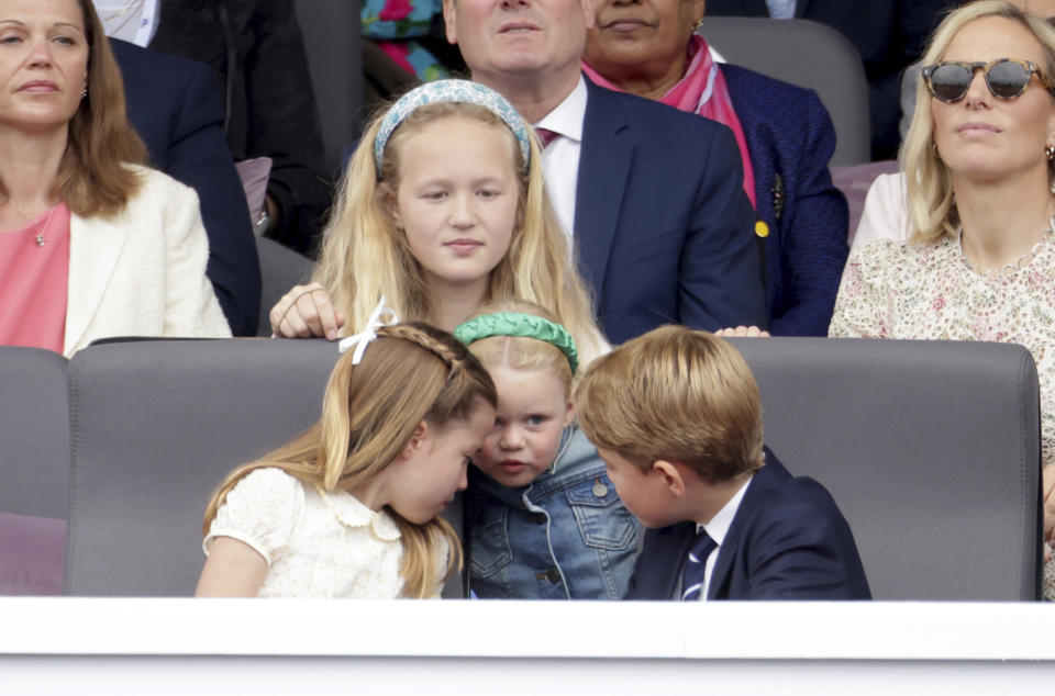 Savannah Phillips, centre, watches as Mia Tindall, foreground centre, Princess Charlotte, left and Prince George speak, during the Platinum Jubilee Pageant outside Buckingham Palace in London, Sunday June 5, 2022, on the last of four days of celebrations to mark the Platinum Jubilee. The pageant will be a carnival procession up The Mall featuring giant puppets and celebrities that will depict key moments from Queen Elizabeth II’s seven decades on the throne. (Chris Jackson/Pool Photo via AP)