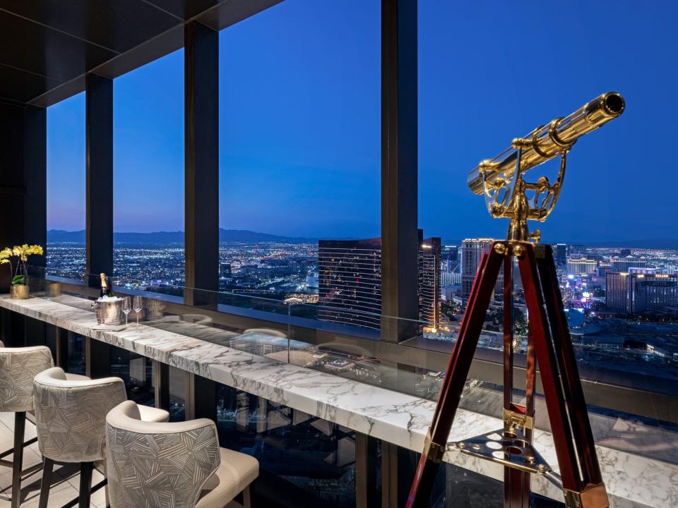 bar seating facing floor to ceiling windows with a view of Las Vegas with a telescope