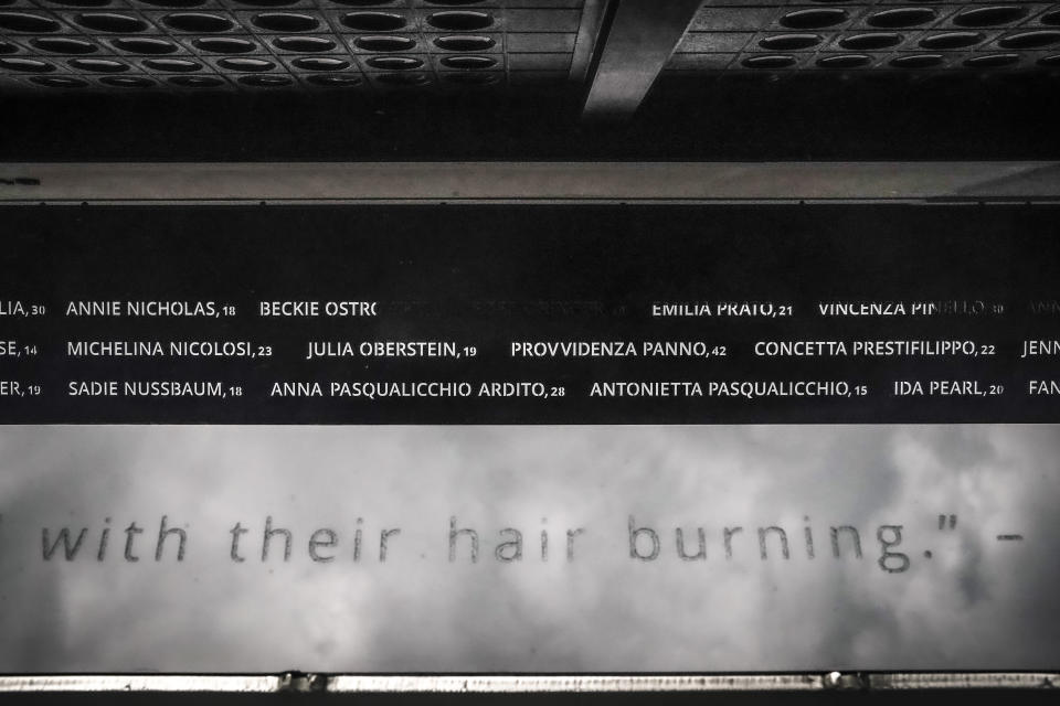 Names engraved in a metal overhang section of the Triangle Shirtwaist Memorial, wrapping the first story of New York University's biology building, are shown reflected in mirroring panels along a sidewalk, Tuesday Oct. 10, 2023, in New York. The building is the site where 146 people, mostly immigrant girls and women, were killed in a 1911 clothing factory fire. (AP Photo/Bebeto Matthews)