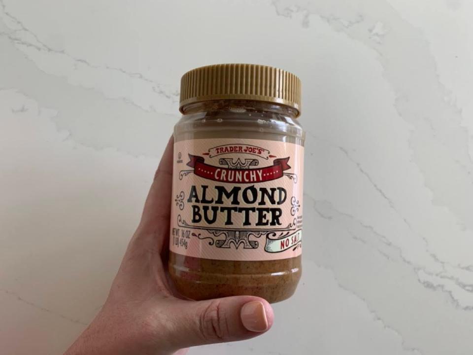 A jar of Trader Joe's crunchy almond butter on a marble countertop.