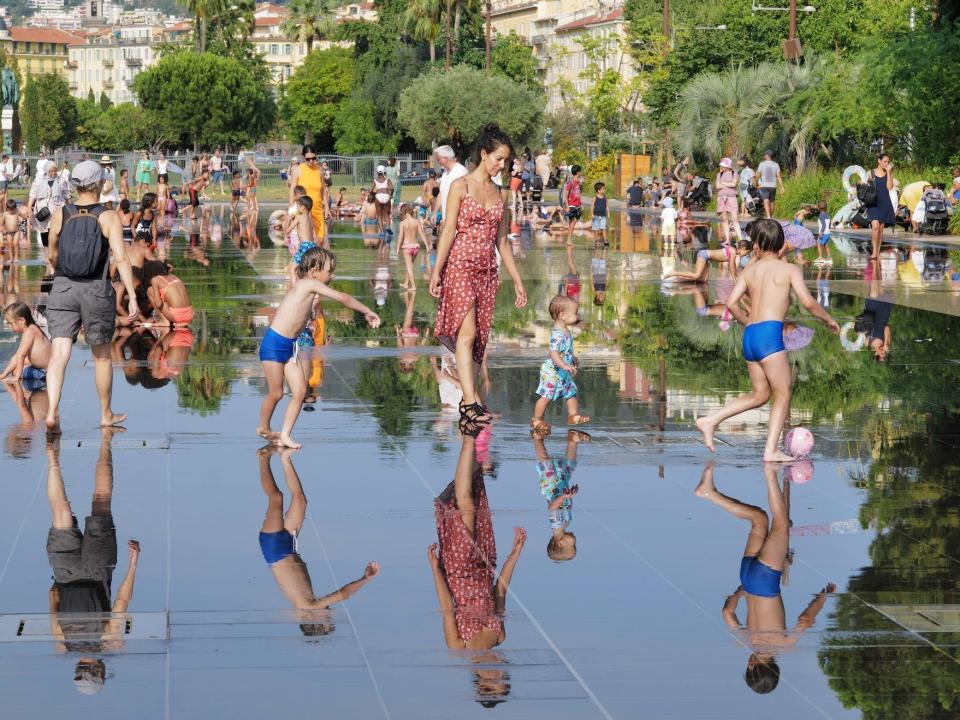 People are walking barefoot in a large water fountain in the sun.