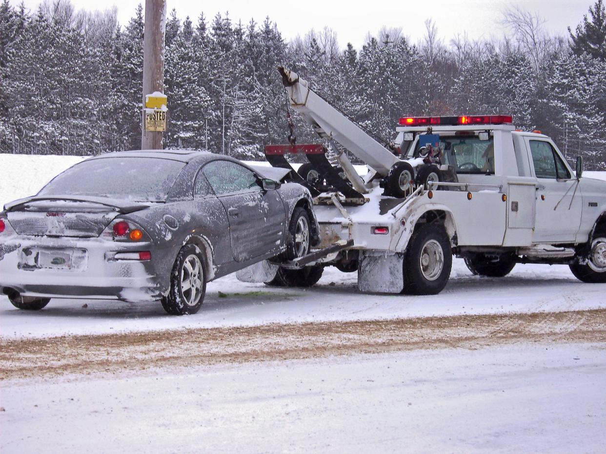 Tow truck hauling a wrecked car away in winter.