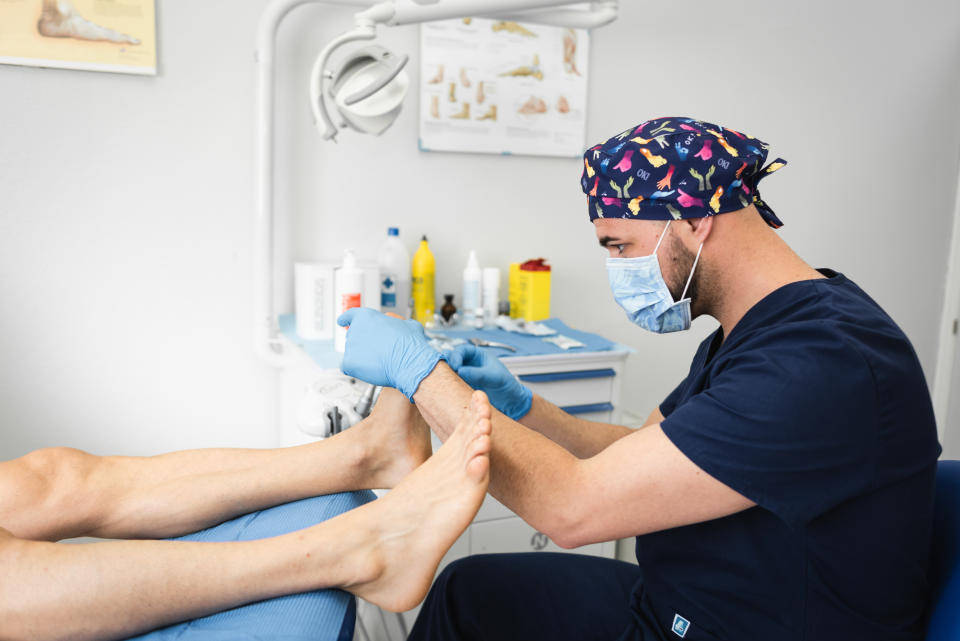 A podiatrist in a gown examines a patient's foot in a clinic