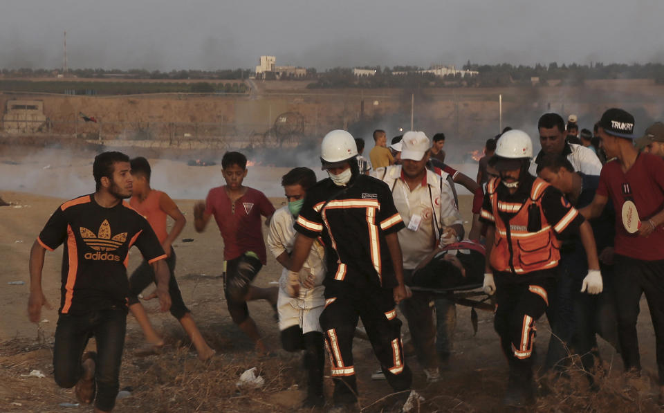 Medics evacuate their wounded colleague, who was shot in his chest, from near the fence of Gaza Strip border with Israel during a protest east of Khan Younis, southern Gaza Strip, Friday, Oct. 5, 2018. Israeli forces shot dead three Palestinians, including a 13-year-old boy, as thousands of people protested Friday along the fence dividing the Gaza Strip and Israel, Gaza's Health Ministry said. (AP Photo/Adel Hana)