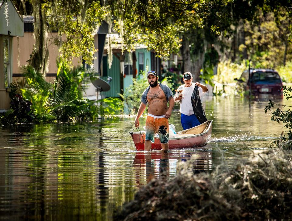 Brad Moore helps his father Felix Atkinson carry out some of his belongings in a canoe from his flooded home in Peace River Village on the Peace River In Bartow Fl. Monday October 3,2022Ernst Peters/.The Ledger