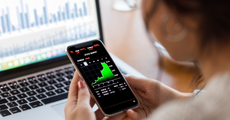 A young woman looks at the performance of her investments on her phone.