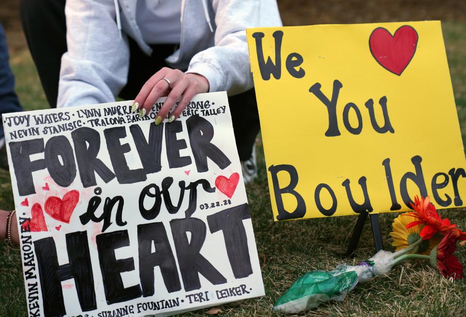 An attendee at a vigil to remember the 10 killed in Monday's shooting at a King Soopers grocery store in Boulder, Colo., sets out a sign.