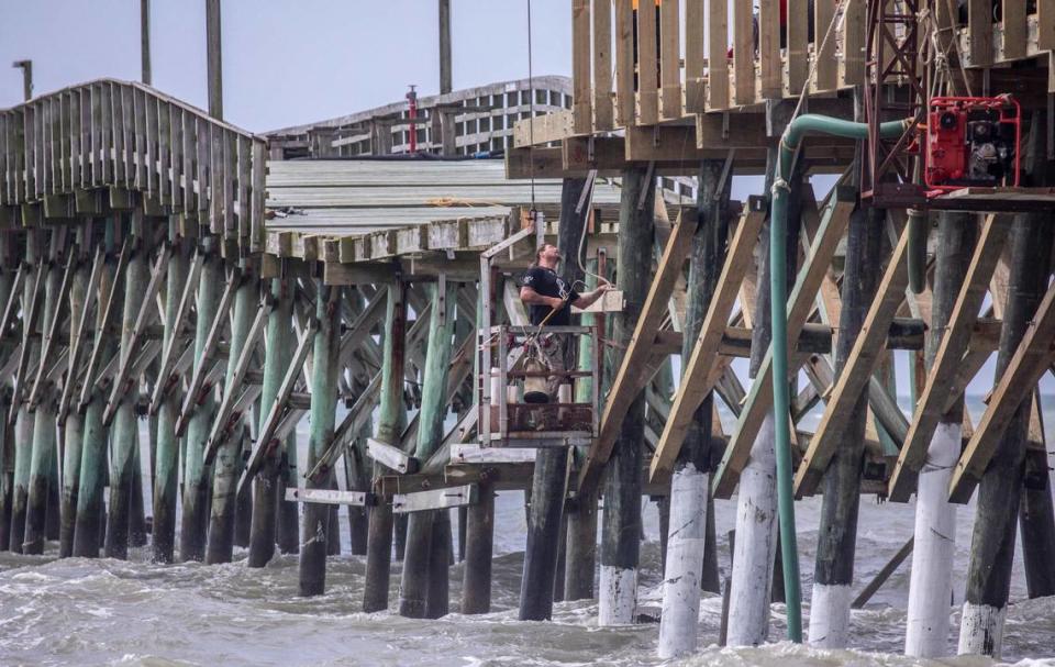 A worker hangs from a crane to work on repairs of the Cherry Grove Pier in North Myrtle Beach, S.C. The pier is undergoing repairs after the landmark was damaged from Hurricane Ian in September 2022. June 23, 2023. JASON LEE/jlee@thesunnews.com