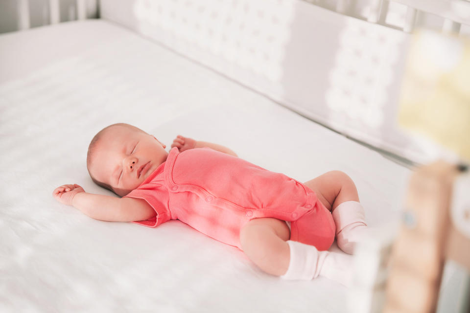 Infant sleeping peacefully on a crib mattress, dressed in a plain onesie