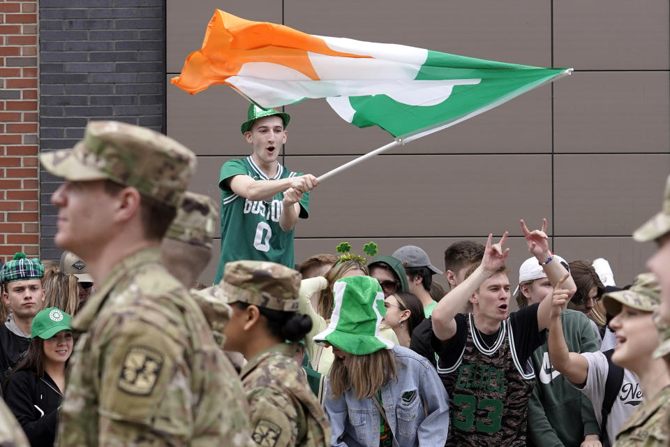 FILE - A spectator, top, waves a flag that features a likeness of a shamrock as members of the Boston University ROTC program, left, march past during the St. Patrick's Day parade, Sunday, March 20, 2022, in Boston's South Boston neighborhood. The day honoring the patron saint of Ireland is a global celebration of Irish heritage. And nowhere is that more so than in the United States, where parades take place in cities around the country and all kinds of foods and drinks are given an emerald hue. (AP Photo/Steven Senne, File)