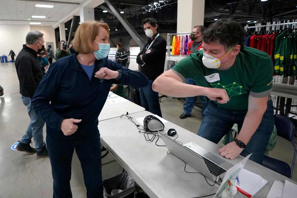 Seattle Mayor Jenny Durkan, left, greets a worker at a volunteer check-in station, Saturday, March 13, 2021, on the first day of operations at a mass COVID-19 vaccination site at the Lumen Field Events Center in Seattle, which adjoins the field where the NFL football Seattle Seahawks and the MLS soccer Seattle Sounders play their games.