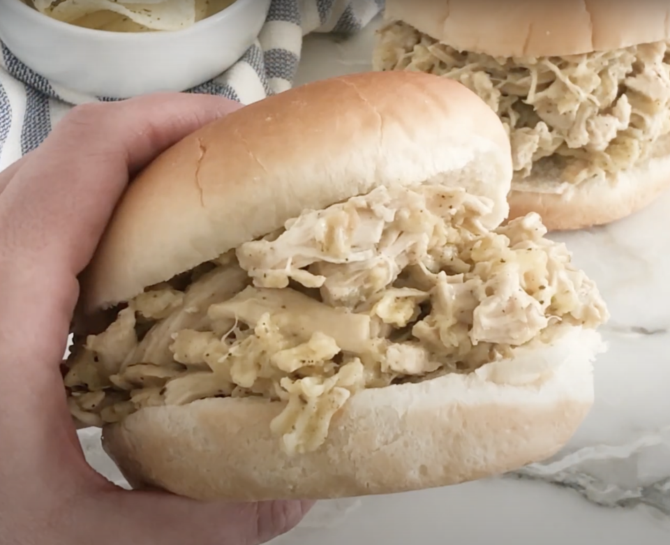 A person&#39;s hand holding a shredded chicken sandwich