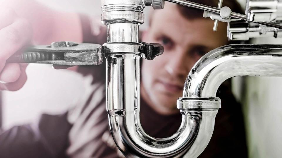 Plumber using a wrench to tighten a siphon under a sink.