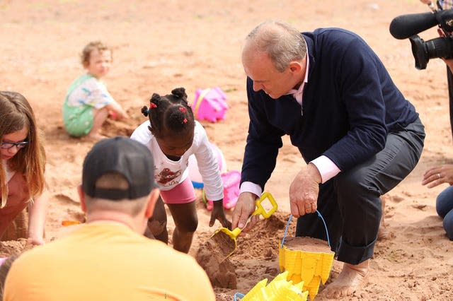 Sir Ed Davey crouches as he builds a sandcastle with a little girl