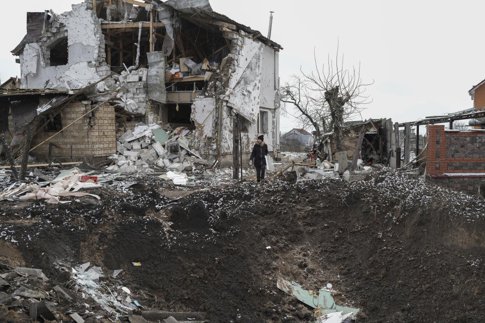 A woman stands on top of a crater next to a destroyed house after a Russian rocket attack in Hlevakha, Kyiv region, Ukraine, Thursday, Jan. 26, 2023. (AP Photo/Roman Hrytsyna)