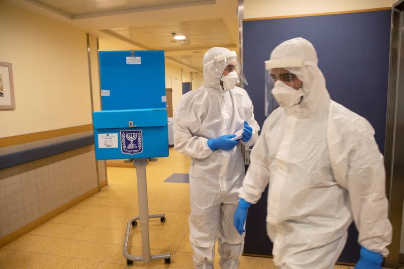 Hospital employees stand next to a mobile voting booth and box as they make their way to assist patients in a ward for the treatment of the coronavirus disease (COVID-19), to vote in Israel's general election, at Sheba Medical Center in Ramat Gan