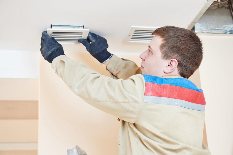 A man in black gloves removes a vent cover.