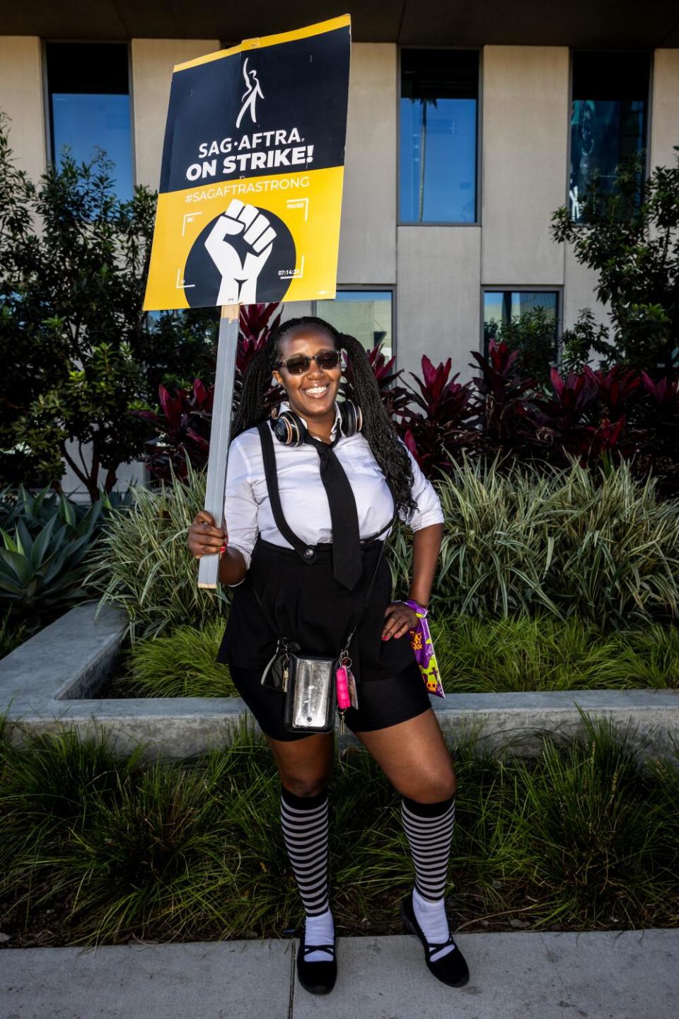 A woman dressed as a goth schoolgirl while smiling and holding a picket sign