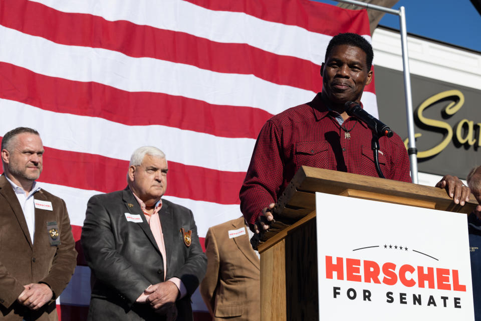 Herschel Walker stand behind a podium with a sign reading: Herschel for Senate.