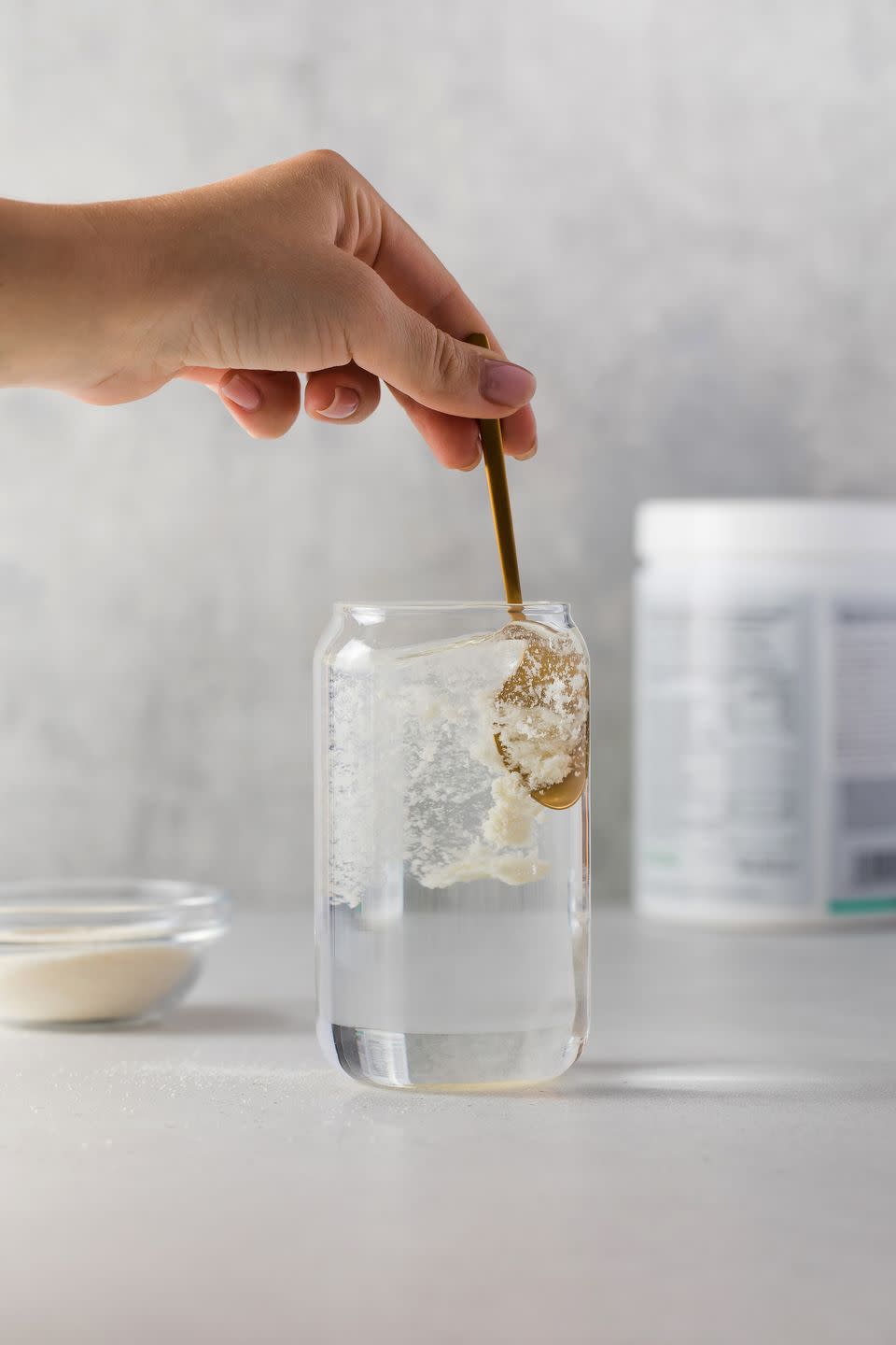 hydrolyzed collagen powder is added with a spoon to a transparent glass of water on a grey background the concept of health, anti aging dietary supplements