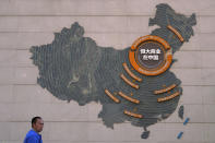 A custodian stands near a map showing Evergrande development projects in China on a wall in an Evergrande city plaza in Beijing, Tuesday, Sept. 21, 2021. Global investors are watching nervously as the Evergrande Group, one of China's biggest real estate developers, struggles to avoid defaulting on tens of billions of dollars of debt, fueling fears of possible wider shock waves for the Chinese financial system. (AP Photo/Andy Wong)