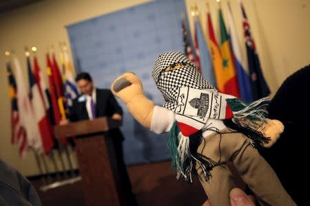 Israel's U.N. Ambassador Danny Danon (L) speaks during a press briefing as a reporter holds a doll that Danon brought to the briefing that he said was part of a shipment that Israel recently stopped of "thousands of dolls dressed as terrorists, with stones in hand, destined for children in the West Bank" before a United Nations Security Council meeting on the Middle East at U.N. headquarters in New York, January 26, 2016. REUTERS/Mike Segar