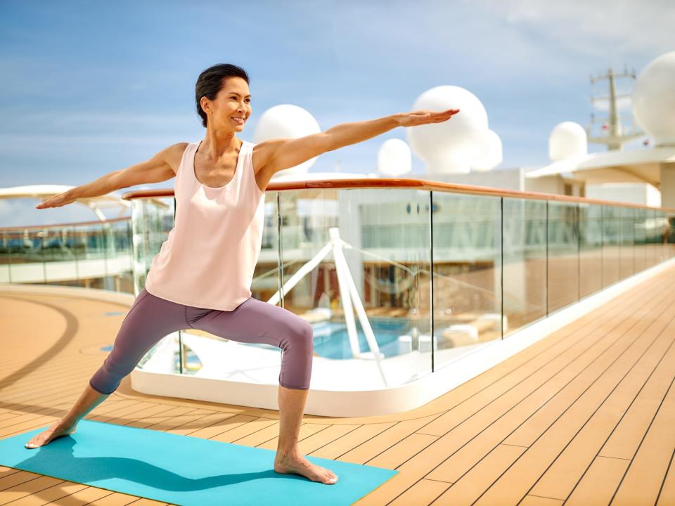 A woman in exercise gear holding a pose on a yoga mat on the deck of The World.