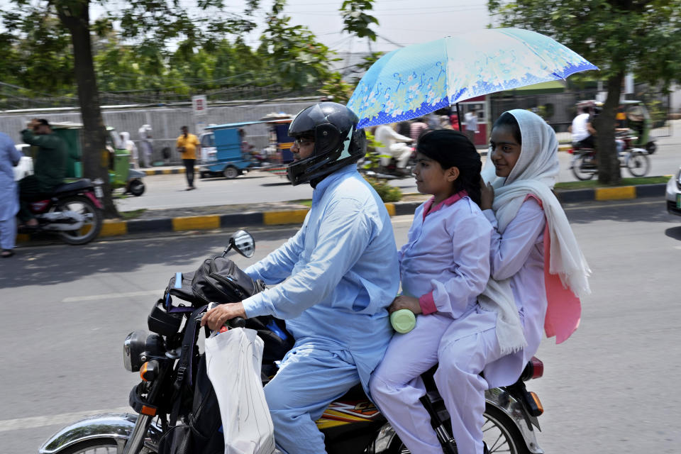 Students use an umbrella to protect themselves from heat as they travel on a bike after attending their school, in Lahore, Pakistan, Tuesday, May 21, 2024. Authorities in Pakistan on Tuesday urged people to stay indoors as the country is hit by an extreme heat wave that threatens to bring dangerously high temperatures and yet another round of glacial-driven floods. (AP Photo/K.M. Chaudary)