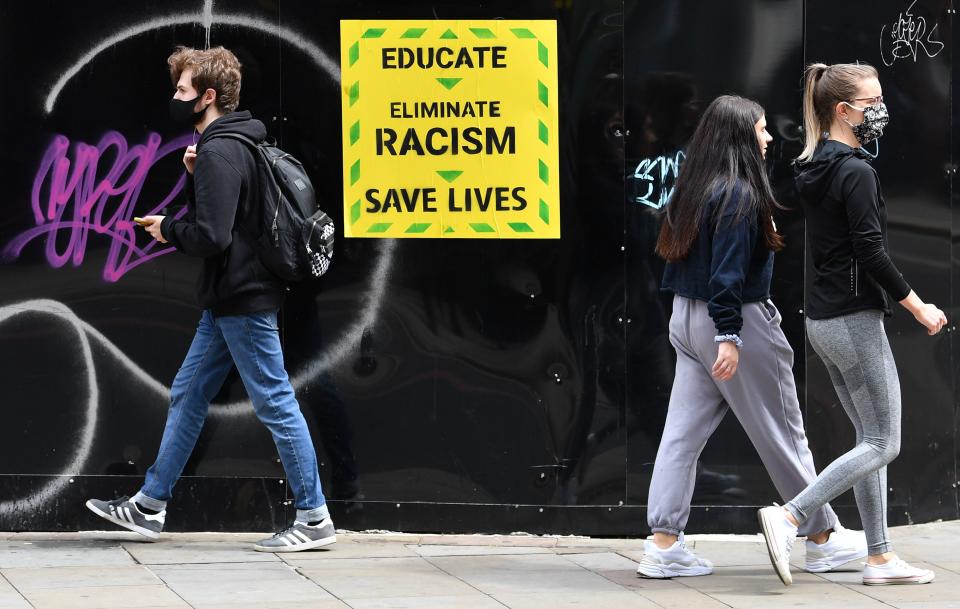 Pedestrians wearing PPE (personal protective equipment), including a face mask as a precautionary measure against COVID-19, walk past an anti-racism poster in the them of the British government's Coronavirus slogan, near a demonstration in Manchester, northern England, on June 6, 2020, to show solidarity with the Black Lives Matter movement in the wake of the killing of George Floyd, an unarmed black man who died after a police officer knelt on his neck in Minneapolis. - The United States braced Friday for massive weekend protests against racism and police brutality, as outrage soared over the latest law enforcement abuses against demonstrators that were caught on camera. With protests over last week's police killing of George Floyd, an unarmed black man, surging into a second weekend, President Donald Trump sparked fresh controversy by saying it was a "great day" for Floyd. (Photo by Paul ELLIS / AFP) (Photo by PAUL ELLIS/AFP via Getty Images)